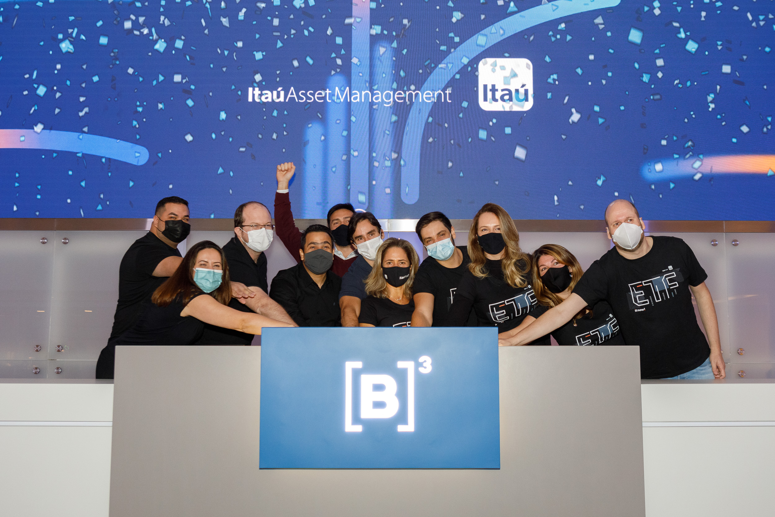 Grupo de pessoas usando máscara unem as mão em toque de campainha para comemorar estreia do novo ETF.