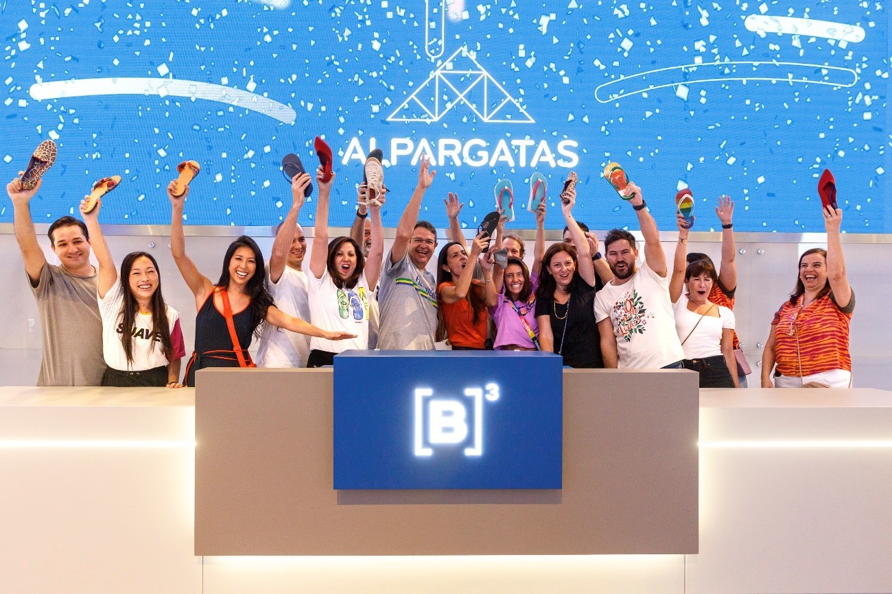 Grupo de pessoas toca a campainha unindo as mãos no púlpito da B3 comemorando o Follow On da Alpargatas.