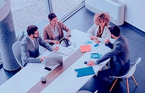 Four people in a meeting around a conference table in a modern office environment.